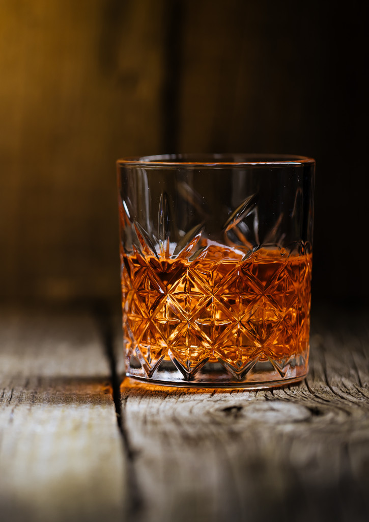 Un verre de rhum posé sur un vieux parquet dans une lumière diffuse mais projetée.